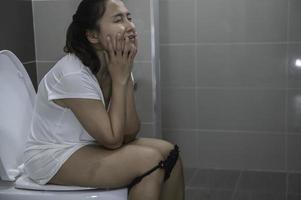 tener problemas con excreción concepto, un asiático mujer se sienta en el baño cuenco, estreñimiento y un largo hora en el baño. foto