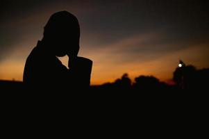 silueta joven asiático musulmán hombre Orando en puesta de sol, ramadán festival concepto foto