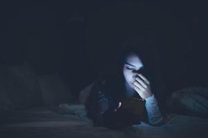 mujer asiática jugando en el teléfono inteligente en la cama por la noche, gente de Tailandia, adicto a las redes sociales foto
