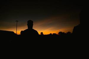 silueta joven asiático musulmán hombre Orando en puesta de sol, ramadán festival concepto foto