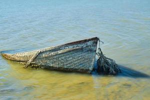 Old abandoned boat, sunken near the shore, sunken or abandoned boat near the sea. Water pollution, environmental problems and garbage pollution photo