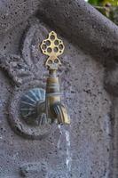 Water flows from an old copper faucet, a vertical shot of a sink in a public place on the street of the old city in Turkey, travel time, an idea for a background photo