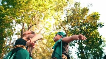 an asian woman and man dancing together while wearing green traditional clothes in the middle of the forest early video