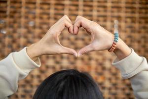 young woman shows her hands above her head making  heart symbol to show friendship love and kindness because heart is symbol of love. Young woman showing love with heart symbol from her hand photo