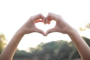 young woman shows her hands above her head making  heart symbol to show friendship love and kindness because heart is symbol of love. Young woman showing love with heart symbol from her hand photo