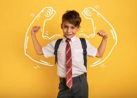 Young boy student acts like a muscled man. Yellow background photo