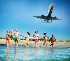 grupo de amigos correr en el mar con aeronave en el cielo. concepto de Hora de verano foto