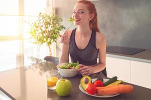 Athletic young red haired woman in the home kitchen eating a healthy salad photo