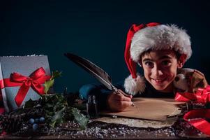 Child with Christmas hat writes a letter to santa claus for gifts photo