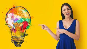Young woman pointing at big stylized light bulb on yellow background. Concept of idea and creativity photo