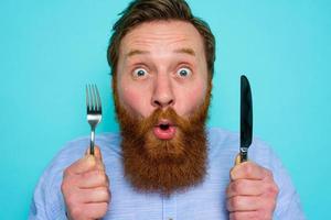 Shocked man with tattoos is ready to eat something with cutlery in hand photo