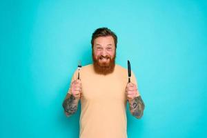 Happy man with tattoos is ready to eat with cutlery in hand photo