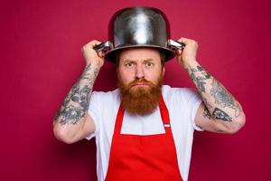 worried chef with beard and red apron plays with pot photo