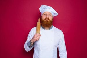 serious chef with beard and red apron chef holds wooden rolling pin photo