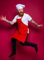 happy chef with beard and red apron jumps photo