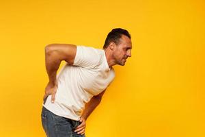 Aching man with back pain. Yellow background photo