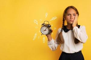 Young child student with ringing alarm clock is lazy going to school. Yellow background photo