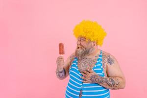 Fat happy man with beard and wig eats a popsicle photo