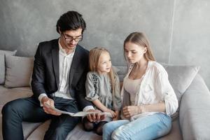 contento pequeño niña lee un libro con su padres foto