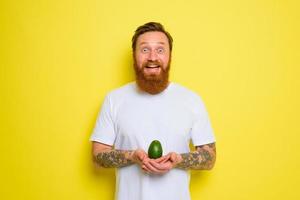 Happy man with beard and tattoos holds an avocado photo