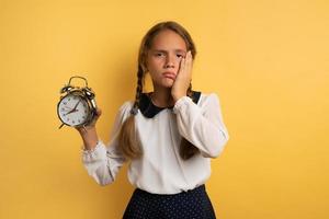 Young child student with ringing alarm clock is lazy going to school. Yellow background photo