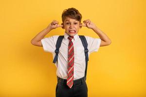 Student Child covers his ears because he does not want to hear noise. Yellow background photo