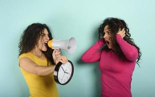 Woman screams with loudspeaker to a friend because is too late. angry expression. cyan background