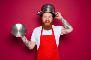 amazed chef with beard and red apron plays with pot photo