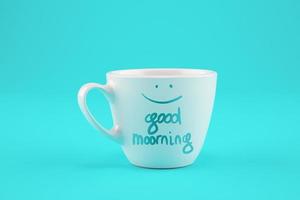 White cup of coffee on a cyan background with a wish for a good day. photo