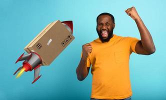 Black man is happy to receive a package. Concept of fast delivery like a rocket. cyan background photo