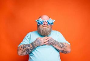 Fat amazed man with beard, tattoos and sunglasses is surprised for something photo