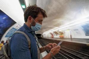 hombre Espere para el subterraneo y plan su viaje con teléfono inteligente foto