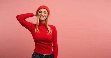 rubia niña sonrisas con rojo sombrero y cárdigan. rosado antecedentes para blanco espacio para tu texto foto