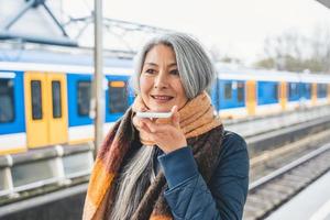 Senior woman send message with a mobile phone and waits for a train photo