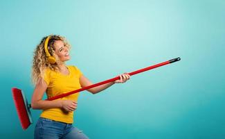 Girl with headset use the broom like a guitar. Cyan background photo