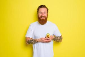 Happy man with beard and tattoos holds an avocado photo