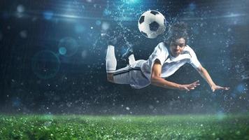 Soccer striker hits the ball with an acrobatic headshot in the air at the stadium photo