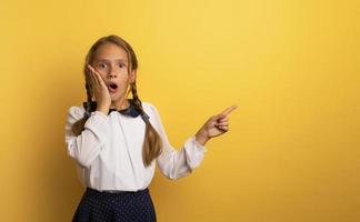 Young student is with shocked expression and indicates something. Yellow background. photo