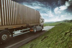 Grey truck moving fast on the road in a natural landscape with cloudy sky photo