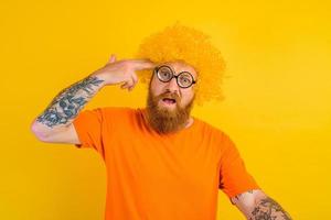 man with beard, yellow wig and glasses does a gun gesture with the hand photo