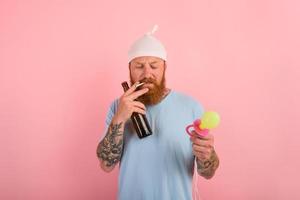 Thoughtful man with beard and tattoos acts like a little newborn baby with beer in hand photo