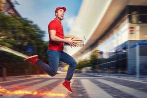 Messenger in red uniform runs on foot really fast to deliver quickly hot pizzas just baked photo
