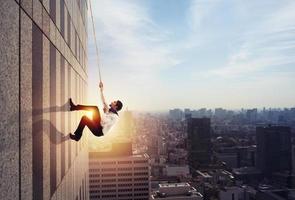 Businessman climbs a building with a rope. Concept of determination photo