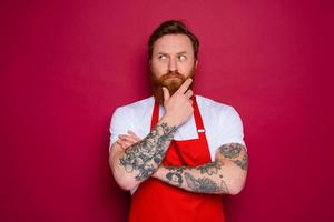 escéptico aislado cocinero con barba y rojo delantal foto