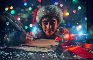 niño con Navidad sombrero escribe un letra a Papa Noel claus para regalos foto