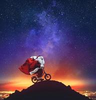 Papa Noel claus en un pequeño bicicleta en el pico de un montaña debajo el estrellas foto