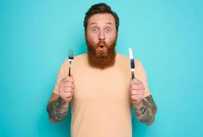 Man with tattoos is ready to eat something with cutlery in hand photo