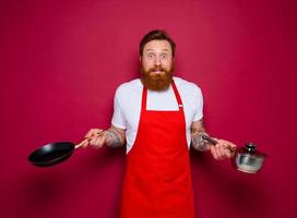 afraid chef with beard and red apron cooks with pan and pot photo