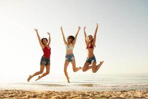 contento sonriente amigos saltando a el playa foto