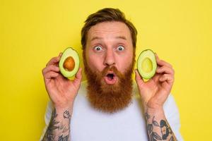 Amazed with beard and tattoos holds an avocado photo